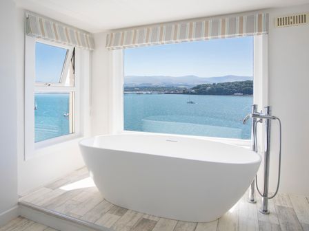 A bathroom with a freestanding bathtub and large windows overlooking a body of water at Glan Dwr Bach in Glyn Garth