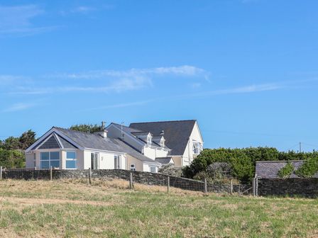 A countryside house with stone walls and a grassy field under a clear blue sky at Glanrhyd Isaf in Llanfair Yn Neubwll