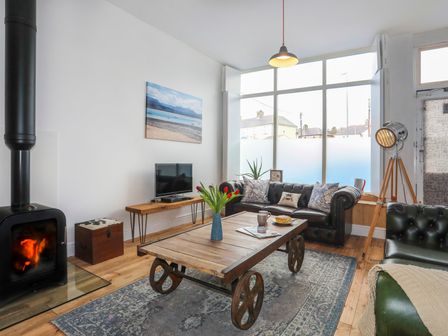 A living room with a wood burning stove and leather sofas at Gwalia Stores in Beaumaris