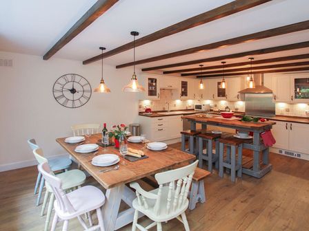 A kitchen and dining area with wooden chairs around a dining table and stools at a kitchen island at Gwyndy Bach in Beddgelert