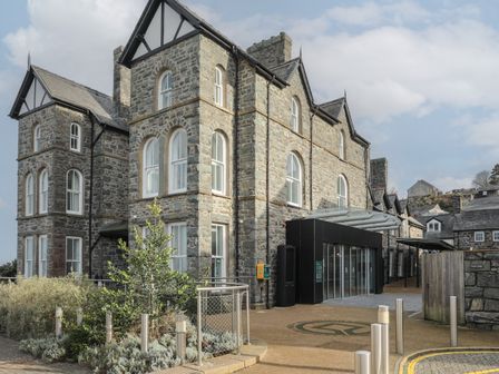 A stone building with arched windows and a modern entrance with glass doors at Harlech Apartments Matholwch in Harlech