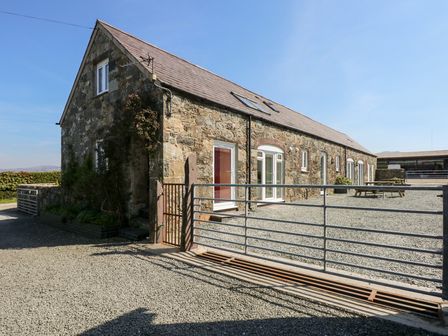 A stone building with a slate roof and metal gate in front at Hendre in Pontllyfni