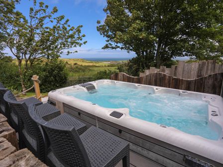 An outdoor hot tub with black chairs around it and a view of fields trees and the sea at Hen Gilfach in Llanfairyngnhornwy