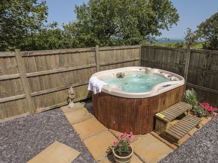 An outdoor hot tub with steps and flowers around it in a fenced area at Hen Gilfach Stable in Llanfairyngnhornwy