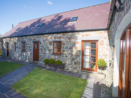 A stone building with wooden doors and windows a small lawn and paved walkway at Hen Stabl Llandwrog
