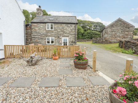 A gravel garden with stepping stones wooden fence potted plants and stone buildings in the background at Little House in Llandecwyn
