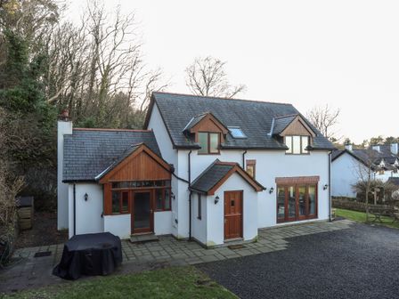 A two story white house with dark roof and wooden trim surrounded by trees and grass at Isfryn in Pentraeth