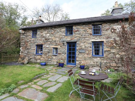 A stone cottage with blue window frames and door a stone pathway and outdoor table with chairs in a garden at Llwyn Bedw in Nant Peris