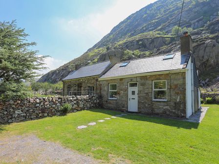 A stone house with a green lawn and a stone wall in front of a mountain at Tan Meredydd in Drws Y Coed