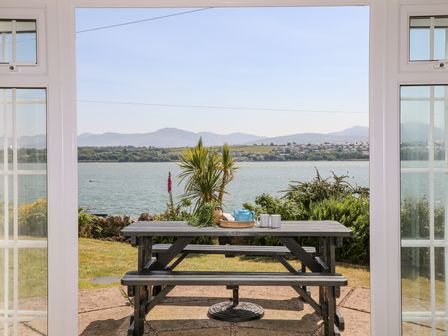 A view of a picnic table with a teapot and mugs outside overlooking water hills and houses at Mermaid Cottage in Brynsiencyn