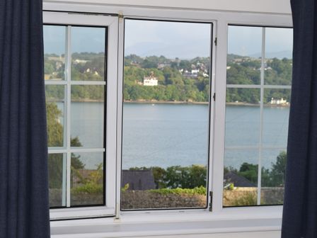 A window with dark curtains showing a river and trees outside at Mews Cottage in Menai Bridge