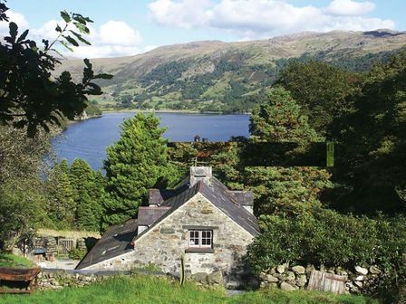 A stone house with slate roof surrounded by trees overlooking a lake and hills at Pantlleni in Nant Gwynant