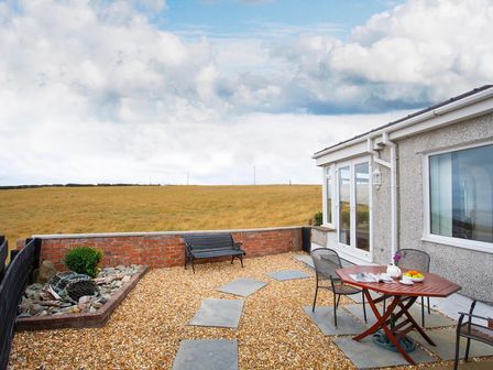 An outdoor patio with a wooden table and chairs and a metal bench at Pen Y Daith in Aberffraw