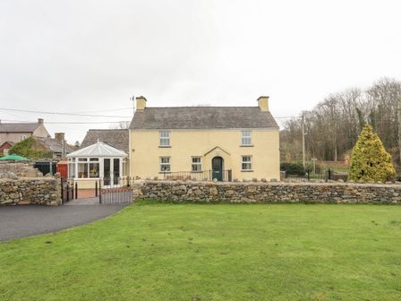 A yellow two-story house with a conservatory and stone wall in front at Plas Cefn Mawr in Llanedwen