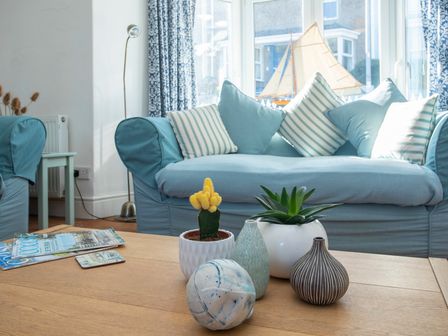 A living room with blue sofas and striped cushions next to a coffee table with plants and decorative items at Plas Mor in Borth-Y-Gest