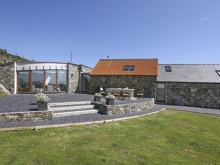 An outdoor patio area with stone steps and seating beside stone buildings with different roof types at Rhyd Angharad Barns in Rhydwyn