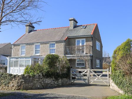 A stone house with a driveway gate and bushes in front at Seiriol View in Moelfre