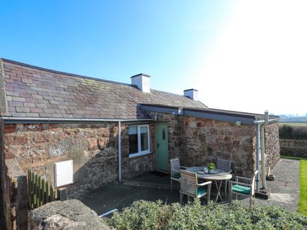 An outdoor patio area with a round table and four chairs next to a stone cottage at Tan Twr Farm Cottage in Dwyran