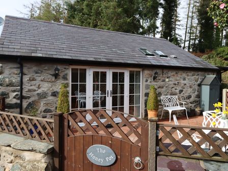 Stone cottage with white doors and outdoor seating behind wooden gate at The Honey Pot in Garndolbenmaen