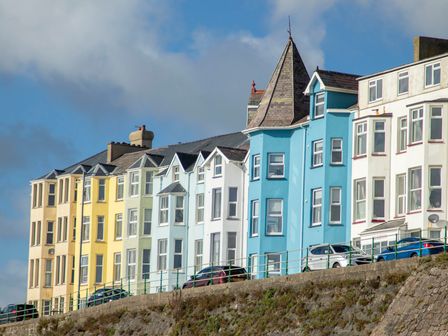 A row of colorful multi-story houses with parked cars along a street at The Towers - Castell in Criccieth