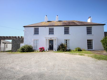 The front view of a white two-story house with a black door and garden bushes at Towyn Lodge in Trearddur Bay