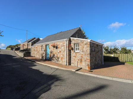 A stone house with a blue door and hanging flower baskets on a paved street at Tyn Towyn - Bwthyn Haf in Trearddur Bay