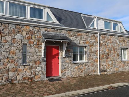Stone exterior of a house with a red door and windows at Tyn Towyn - Ty Coch in Trearddur Bay