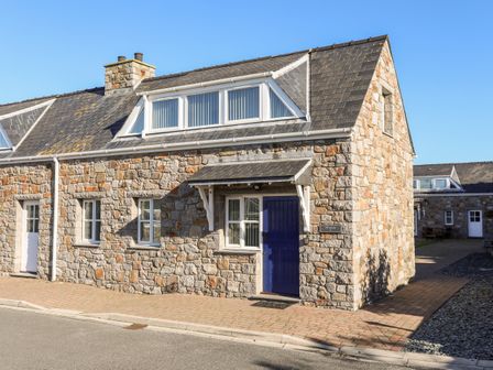 A stone house with a blue door and multiple windows under a clear sky at Tyn Towyn - Ty Glas in Trearddur Bay