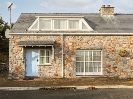 A stone house exterior with blue door and white framed windows at Tyn Towyn - Ty Glas Golau in Trearddur Bay