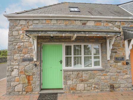 Stone exterior of a building with a green door and a window under a gray tiled roof at Tyn Towyn - Ty Gwyrdd Golau in Trearddur Bay