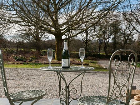 An outdoor metal table and two chairs with a bottle and two glasses on the table in a garden at Tyddyn Morthwyl in Criccieth