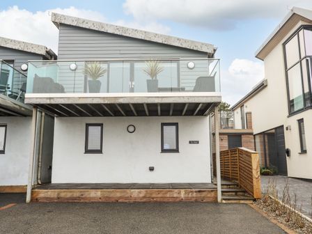 A two story building with a balcony and glass railing at Ty Glyn in Criccieth