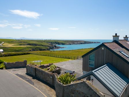 A coastal view with a grassy field and a house with a stone wall near the coast at Ty Nant in South Stack