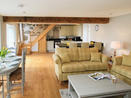 An open living room and kitchen with yellow plaid sofas dining table and wooden staircase at Mulberry Cottage in Pentraeth