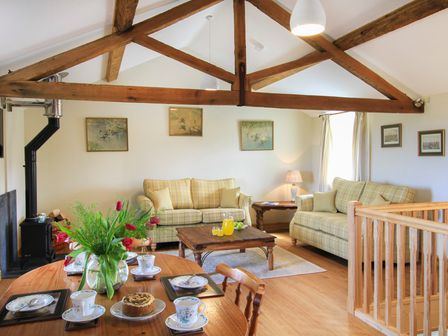 A living area with two sofas a wooden coffee table and a dining table with a vase of flowers and tea set at Partridge Cottage in Menai Bridge