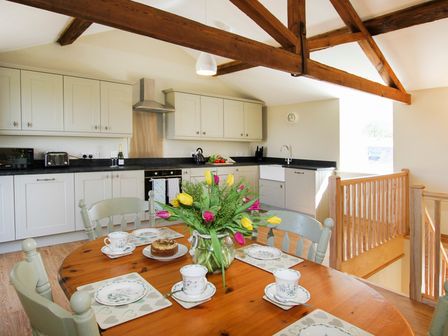 A kitchen and dining area with wooden beams and a table set with flowers and tea cups at Teal Cottage Menai Bridge