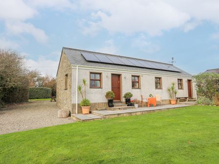 A single story house with solar panels on the roof a small patio with chairs and plants and a grass lawn at Y Beudy in Llanynghenedl