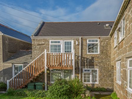 A stone house with wooden staircase and garden at Potters by the Sea in Sennen