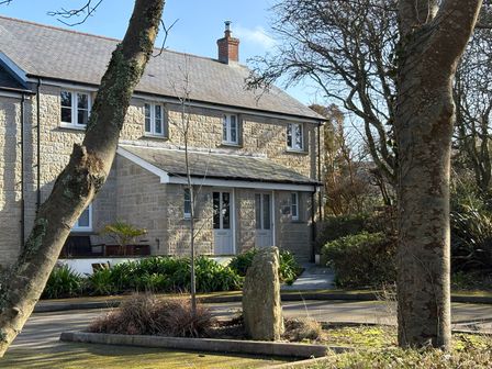 A stone house with two doors surrounded by trees and plants at Tinners Rest in Pendeen