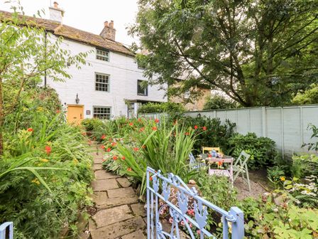 A garden with a stone path leading to a white house with a yellow door and a seating area with chairs and a table at Bonny Bits Cottage Garrigill near Alston