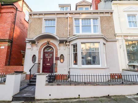 A front view of a two story house with a maroon door and large windows at Livingstone House in Llandudno