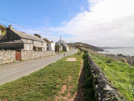 A coastal road with stone cottages on one side and a grassy area with benches overlooking the sea at Virginia Cottage in Portwrinkle near Whitsand Bay