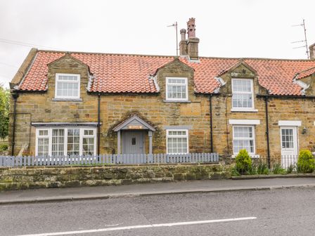 A stone house with orange roof tiles white framed windows and a small front garden with a blue fence at 11A High Street in Burniston