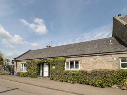 A stone cottage with a white door and windows covered in green ivy at Forge Cottage in Rothbury