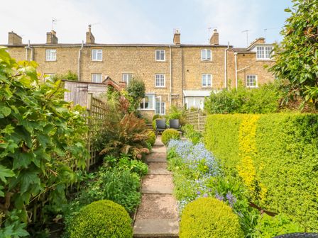 A garden with a stone path leading to chairs and a stone house in the background at Thrower's Cottage in Blockley