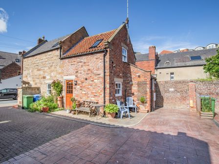 Exterior view of a brick and stone house with a paved patio and outdoor seating at Moor Croft in Whitby