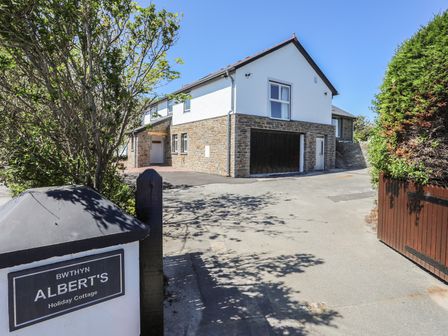 Entrance view of a two story holiday cottage with stone and white walls and driveway at Bwthyn Alberts in Trearddur Bay