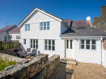A white stone house with a patio table and chairs outside at Stabl Bach in Llanfaethlu