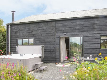 A garden area with a hot tub and outdoor table set beside a black wooden building at The Pig Shed -Sty 2 in Tenbury Wells