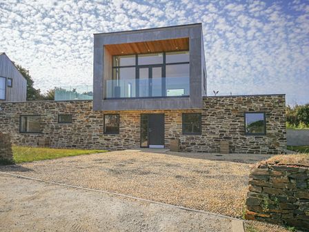 A modern two-story house with stone lower level and large glass windows on the upper level at Idlewild 2 Wheal Turnavore in St Agnes